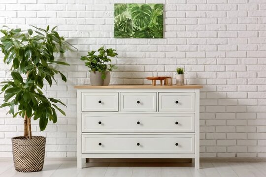 Green houseplant on commode and painting hanging at white brick wall in living room
