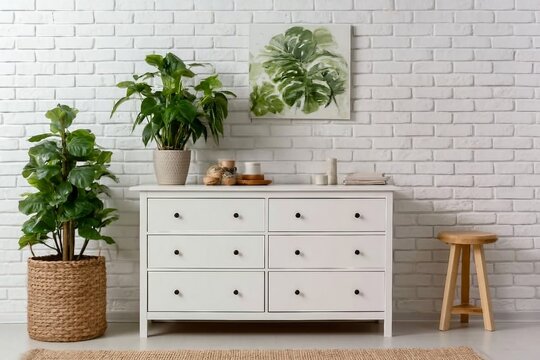 Green houseplant on commode and painting hanging at white brick wall in living room
