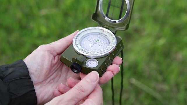 Woman's hand finds its way with a compass in a field against a background of green grass. Compass orientation, travel, adventure, and navigation concepts.
