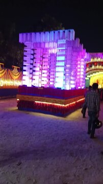 18 October 2023, Howrah, West Bengal, India. Crowd of people visiting a brightly lit Durga Puja pandal at night, admiring the majestic goddess idol and colorful festive decorations.