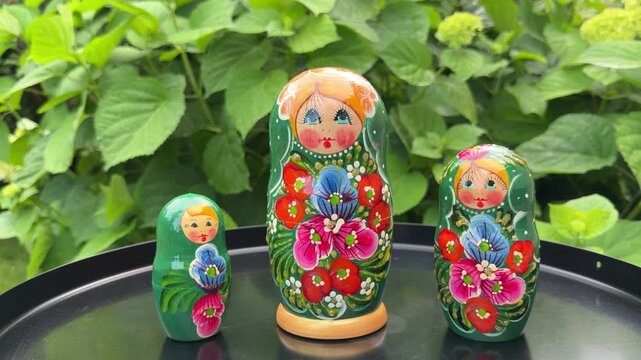Matryoshka Dolls in Nature: A trio of brightly painted Matryoshka dolls, showcasing traditional Russian folk art, are displayed outdoors against a lush green leafy background.