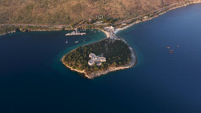 Aerial view of the historic Porto Palermo Castle situated on a green peninsula surrounded by the deep blue waters of the Adriatic Sea in Porto Palermo, Qarku i Vlores, Albania.