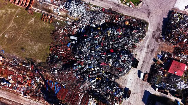 Scrapyard pile with crushed old automobiles. Direct overhead view of a massive mound of recycled metal, vehicle parts and iron waste on industrial concrete ground.