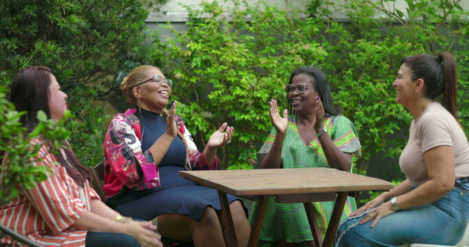 Four women clap and smile in shared excitement during vibrant backyard gathering, celebrating a joyful and uplifting group moment