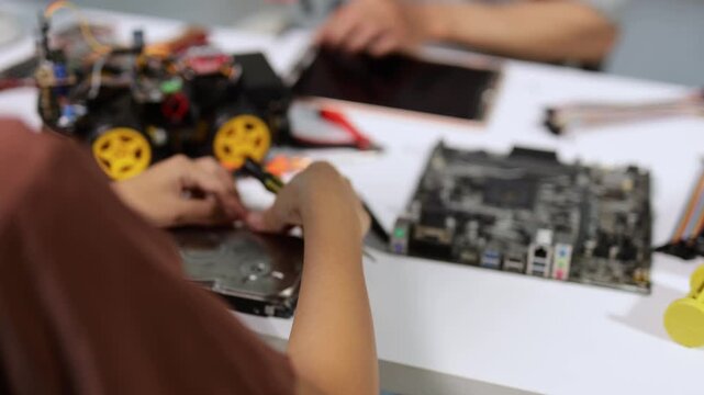 Young engineering students in a laboratory working together on electronics projects, assembling a robotic car and disassembling a computer hard drive on a workbench with various tools
