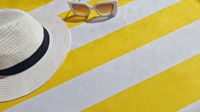 Summer background, vacation, tourism, travel concept. Top view of white straw hat and sunglasses on a yellow and white striped beach towel. Selective focus. Space for text. 