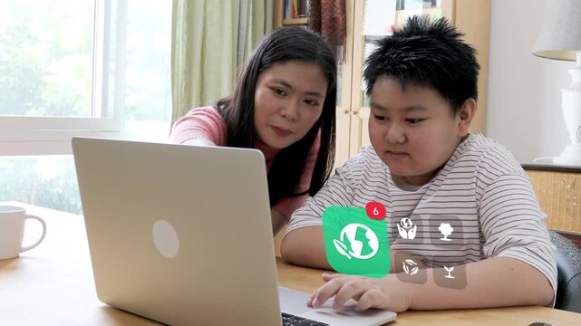 Middle aged East Asian mother shows her child eco conservation on laptop, with 3D tracked green planet leaf badge and recycling tree notification pop up icons.