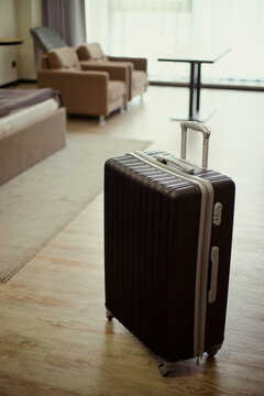 Vertical shot of rolling suitcase standing in hotel room, suggesting family travel check in or vacation stay. Ideal for tourism marketing, hospitality booking, travel service promotion