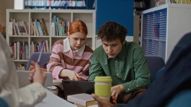 Zoom out of diverse teenagers collaborating on project in library, looking at laptop and taking notes. Perfect for educational marketing and student lifestyle commercials