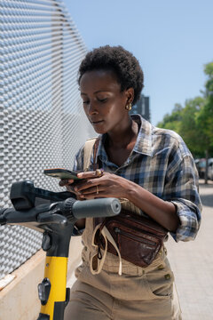 Young Woman Using Phone to Rent E-Scooter on Street