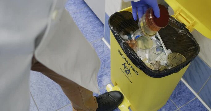 A scientist discards used plastic petri dishes containing bacteria into a laboratory's bio-waste container.