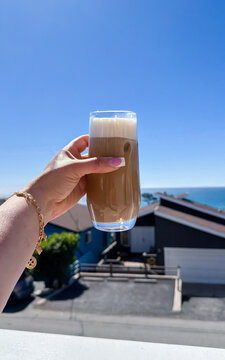 Woman holding iced latte with ocean view on sunny morning