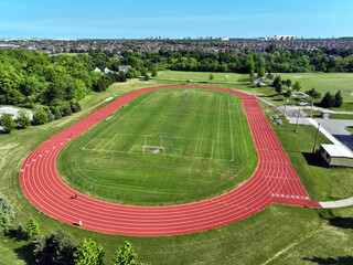 Drone aerial view of a red synthetic running track with eight lanes surrounding a green soccer field in a suburban neighbourhood on a sunny day.  © Barry Lavallee