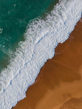 Aerial View Of Ocean Waves Crashing Onto Sandy Beach