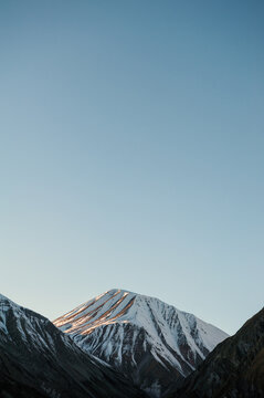 Snow peak Kazbegi rises above rugged terrain under blue sky