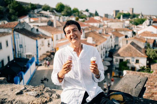 Person Enjoys Ice Cream While Sitting on a Wall in a Town