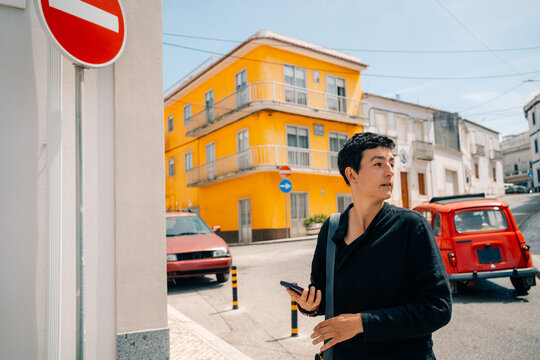Woman Stands Near Road Sign in a City With Buildings and Cars