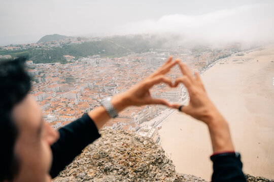 Person Makes Heart Shape With Hands at Coastal View in Cloudy Weather