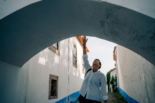 Person Reaches up Under Arch in Narrow Street With White Walls