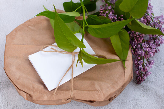 Handmade parcel tied with twine string on grey concrete background, rustic greeting card mockup with blooming flower