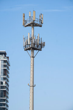 Modern cellular tower with transmitters and antennas for 5G and LTE networks against blue sky. Telecommunication mast equipment near an urban residential building.