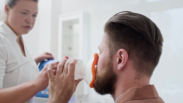 Caucasian man receiving respiratory therapy from female doctor putting inhalation mask on his face. Video suitable for promoting healthcare services and medical treatments