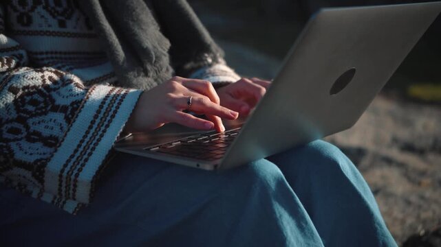 4K close-up video of an anonymous young woman's hands using a laptop in an outdoor park. Remote work, technology and digital lifestyle concept.
