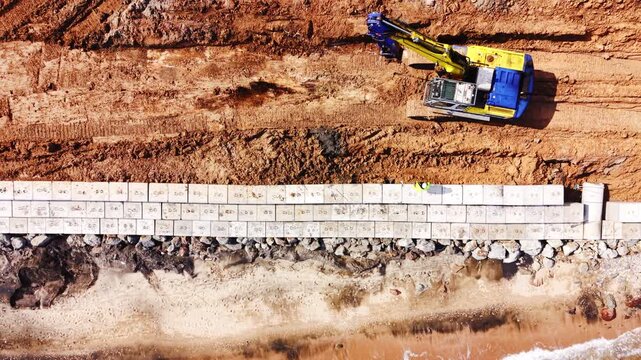 Seawall block installation with concrete mixer truck on Black Sea coast. Excavator, mixer truck, precast block row, rebar stack and soil embankment near shore.