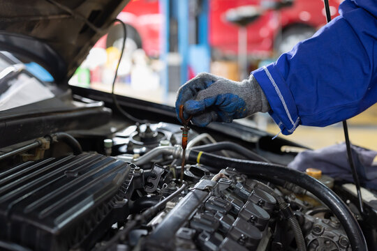 Worker checks oil level in car engine during maintenance session in garage