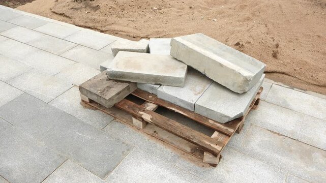 Concrete curbstones and paving slabs stacked on pallet at construction site for urban landscaping and roadworks