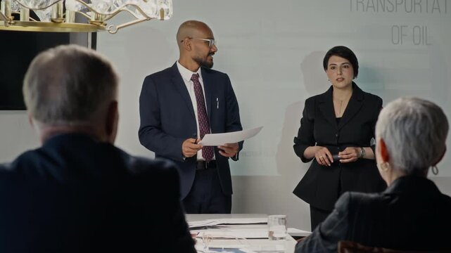 Over the shoulder view of Indian man and Caucasian woman presenting oil transportation report to colleagues in boardroom. Perfect for corporate training videos and energy sector marketing campaigns