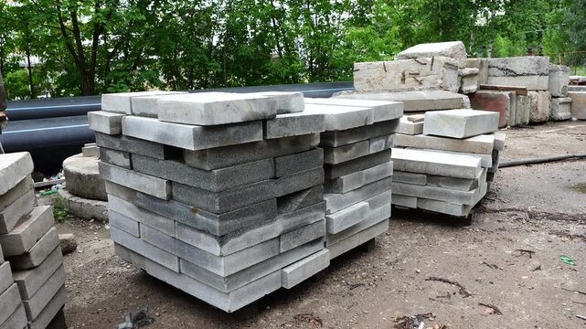 Stacked concrete curbstones and paving slabs stored at construction yard for roadworks and urban landscaping construction