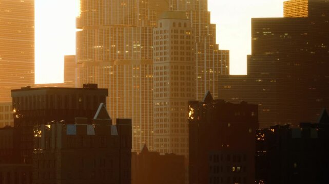 Sun sets over a city skyline filled with tall buildings. The buildings reflect warm light as day turns to night. Streets below are quiet as evening approaches in the urban area.