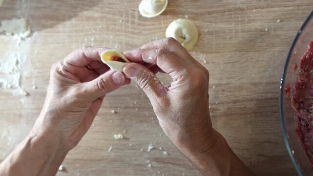 Preparing traditional homemade dumplings by hand with raw dough and meat filling on rustic kitchen table
