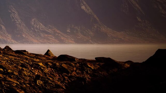 Rocks and mountains are visible near a calm body of water during dusk. The sunlight creates shadows, highlighting the textures of the rocks and the surface of the water.