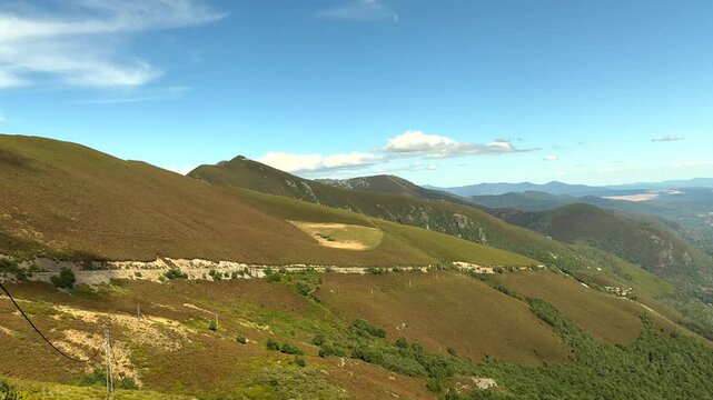 Rolling hills covered with green and brown vegetation. Blue sky with scattered clouds above. Valley stretches far into distance. Mountain ridges fade into haze. No animals or plants identified