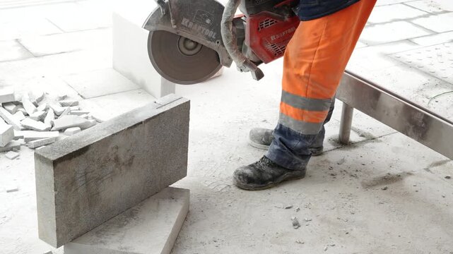 Construction worker in protective clothing cutting concrete block with power tool during building work, renovation and industrial construction process