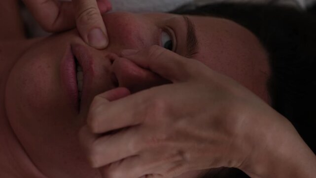 A professional close-up slow-motion video of a wellness facial massage treatment. A professional female masseuse gently and delicately massaging the glowing skin of a young woman's face at a luxury sp
