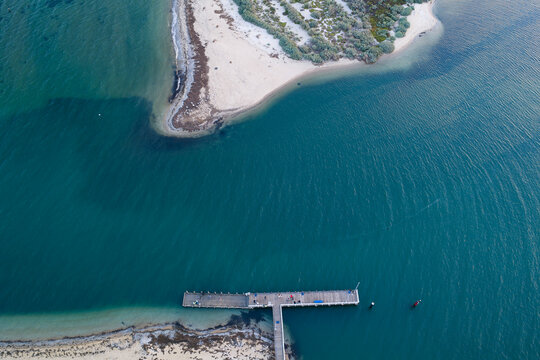 Blue water in a coastal river flowing between a jetty and sandy beach