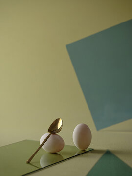 Minimalist still life featuring eggs, a golden spoon on green
