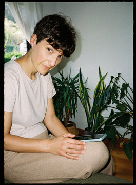 Woman holding phone looking at camera indoors with plants