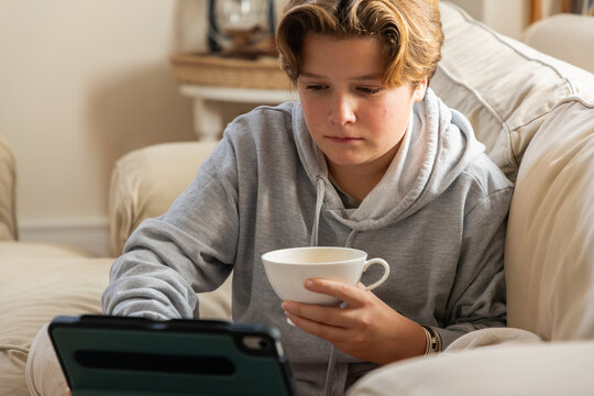 pre teen boy on sofa sipping tea and watching tablet