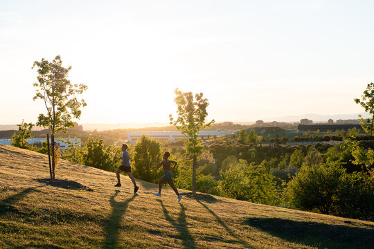 Two people running uphill during sunset in park