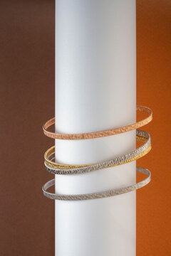 Stack of Mixed Metal Bracelets on Minimalist White Cylinder 