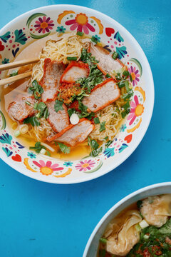 Bowl of noodles with meat and herbs on a blue table