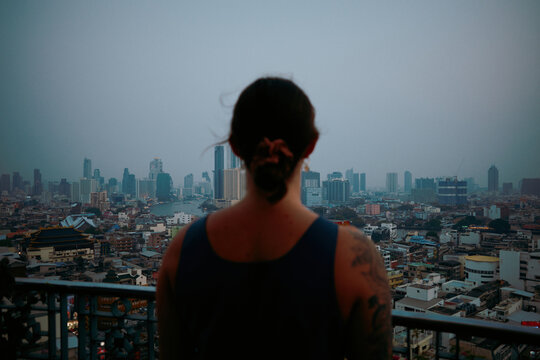 Person looks at city skyline during cloudy evening in urban area
