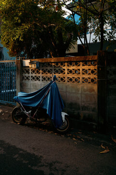 Motorcycle covered in blue cloth near a wall at sunset time