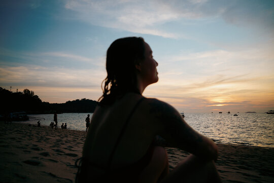 Woman sitting on beach watching sunset over the water