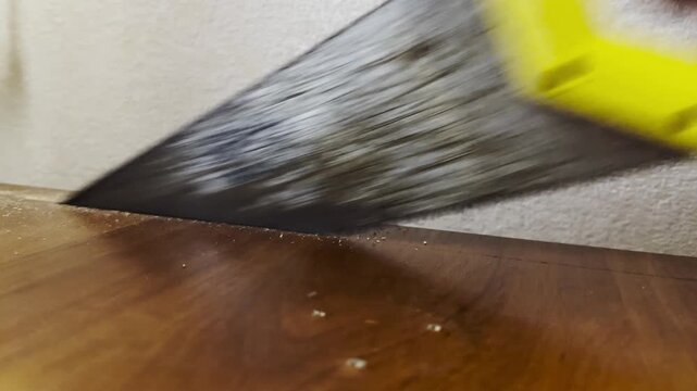 Male hand cuts a wooden surface using a hand saw indoor. The worker carefully saws through the material, performing precise manual work during repair or modification inside the home. Close up