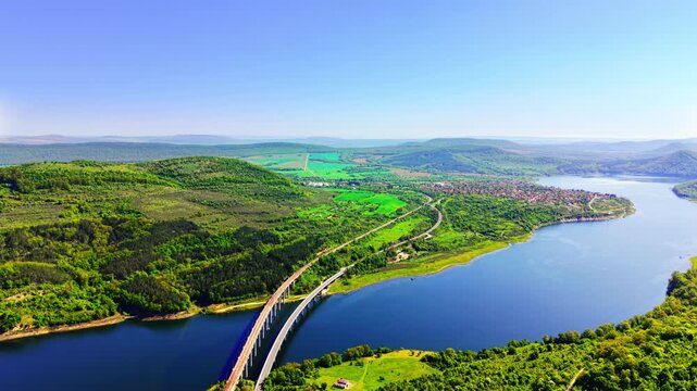 Double bridge infrastructure over a wide water reservoir, Bulgaria. High panoramic view showing parallel concrete viaduct highway curve through green landscape.